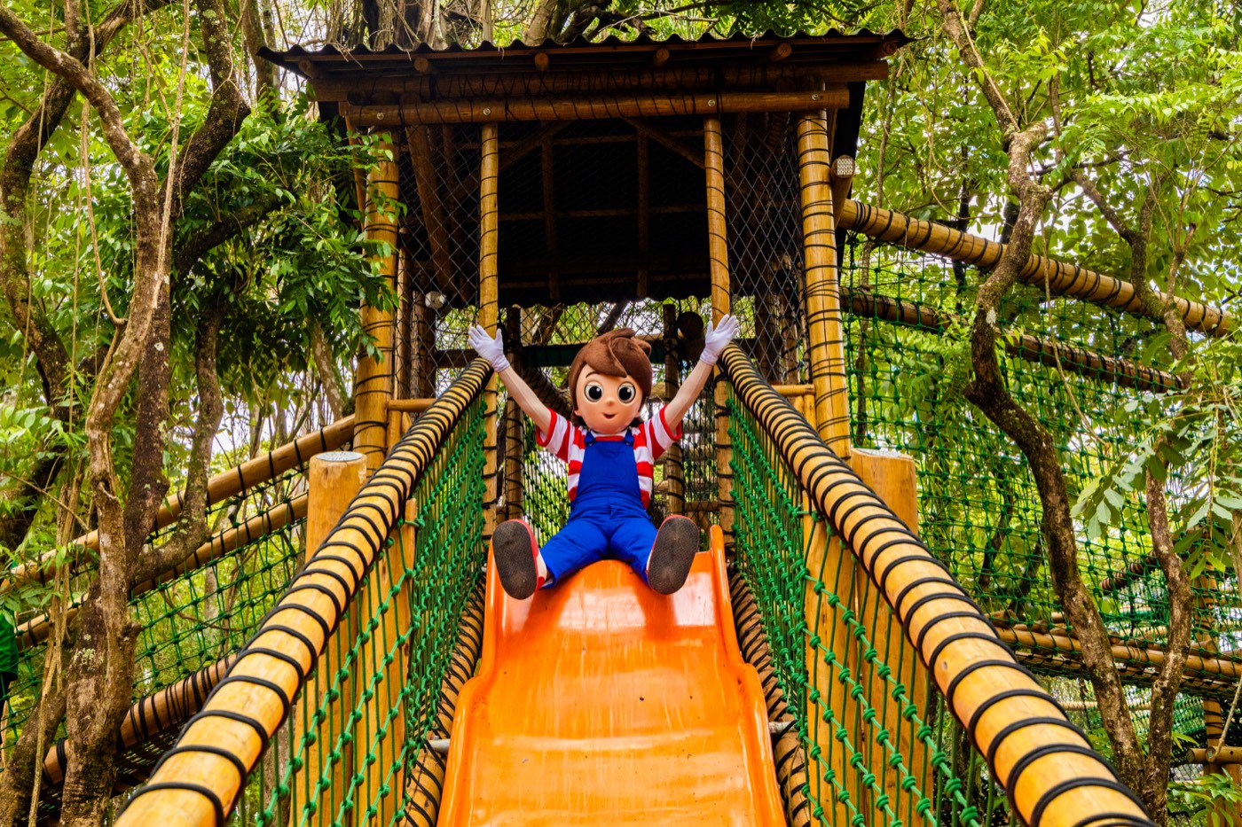 Pedrinho descendo o escorregador do brinquedão As Aventuras de Pedrinho, entre as árvores